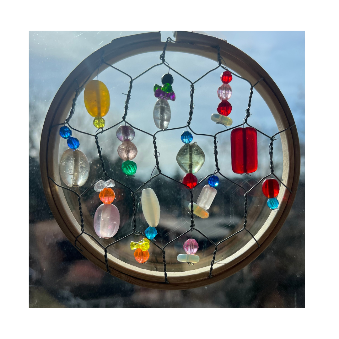 circle suncatcher made of an embroidery hoop and chicken wire with beads, against a window 